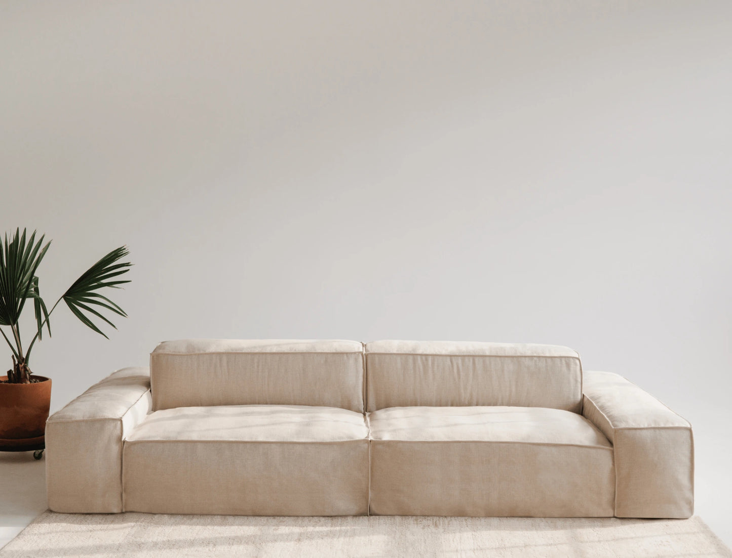 Beige linen sofa in a minimalistic room with a plant on the left.