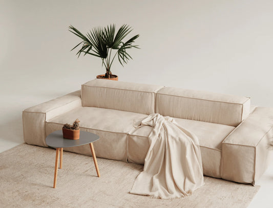 Beige linen sectional sofa with a blanket and small table in a minimalistic room.