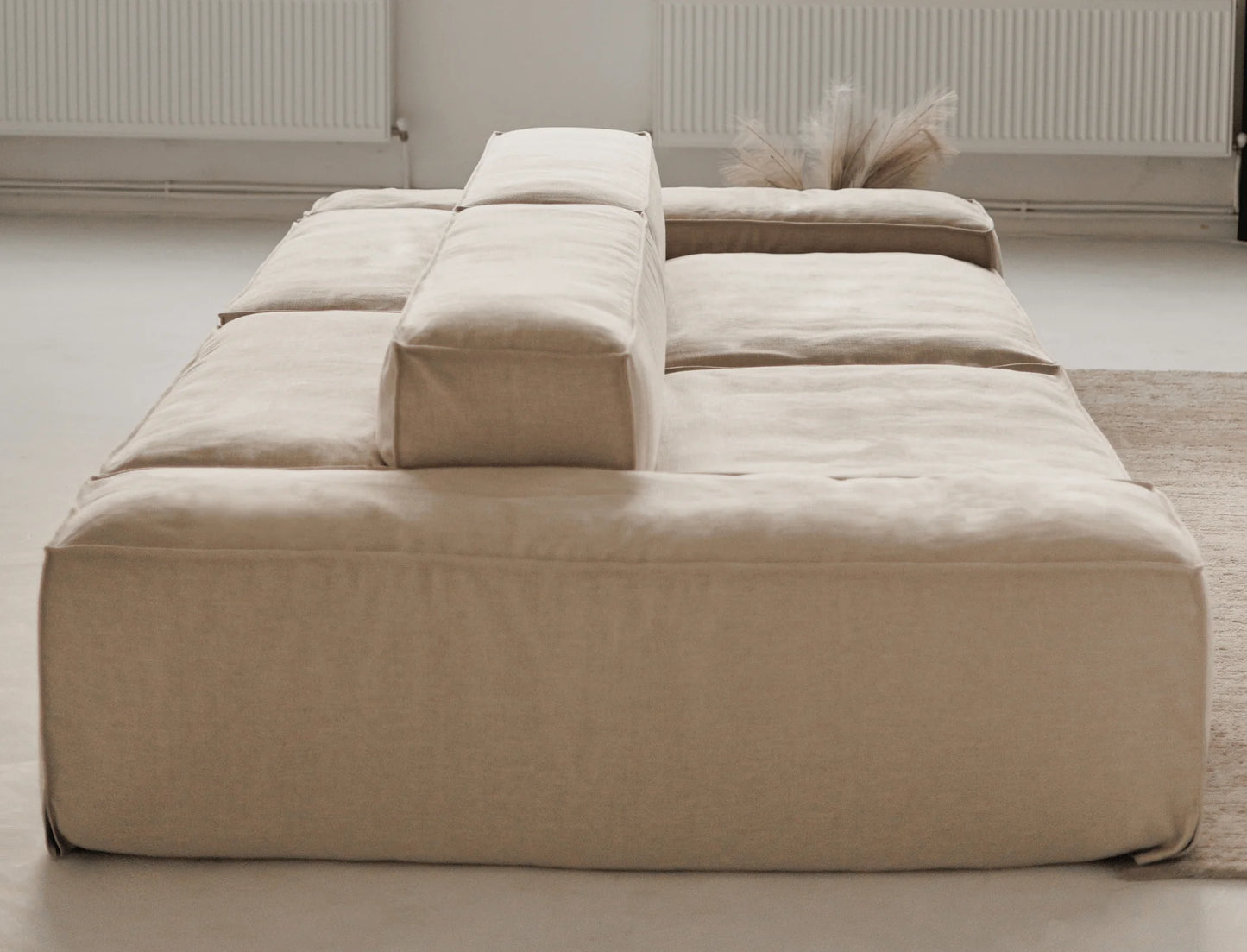 Beige linen sofa in a minimalistic room with a light-colored floor and wall.