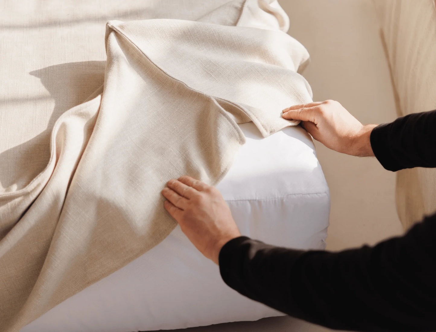Person adjusting a removable cover on a beige sofa