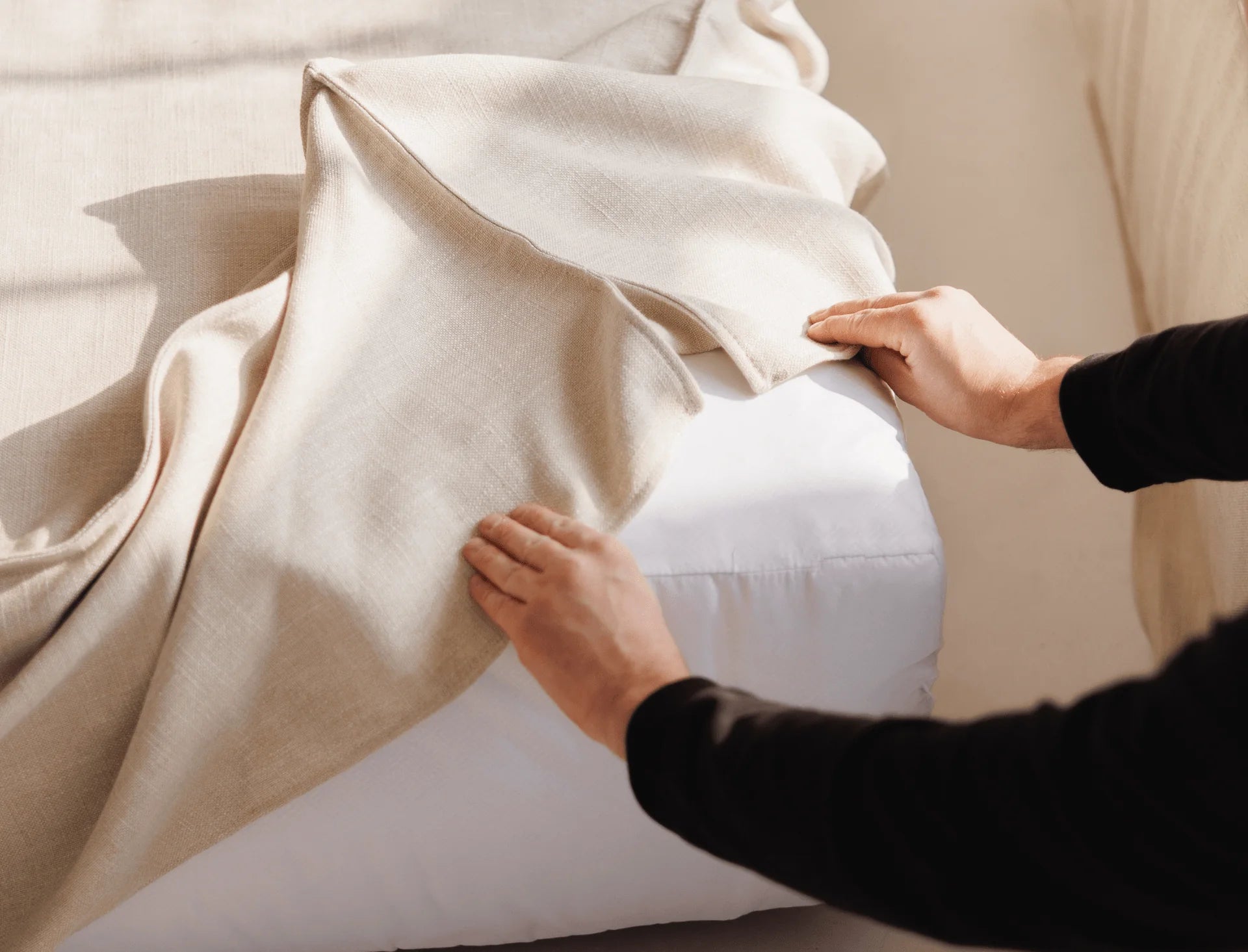 Person adjusting a removable cover on a beige sofa