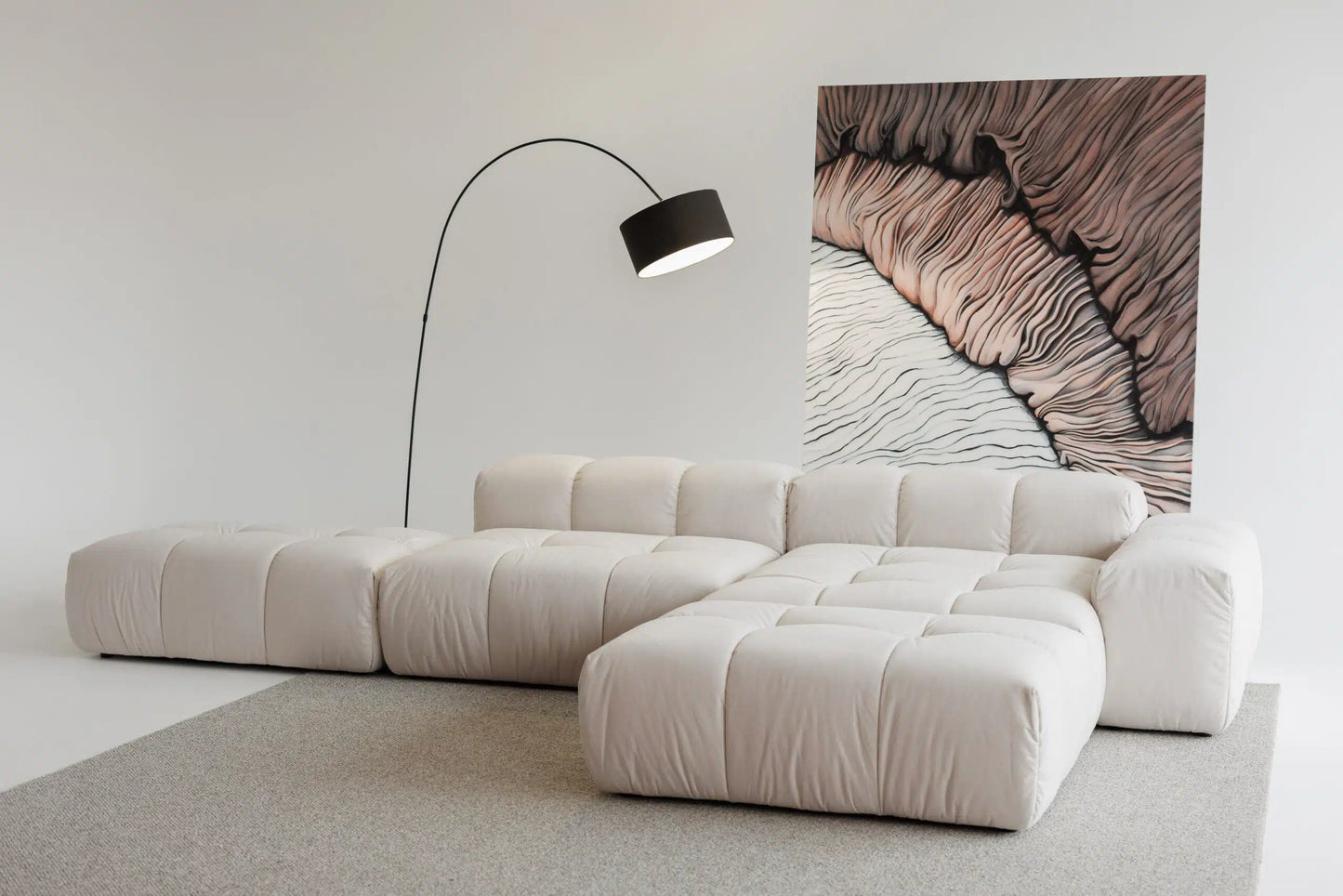 Modern beige sectional sofa in a minimalistic room with a lamp and abstract wall art.