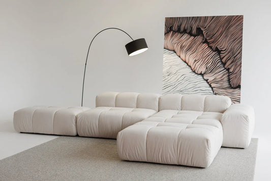 Modern beige sectional sofa in a minimalistic room with a lamp and abstract wall art.