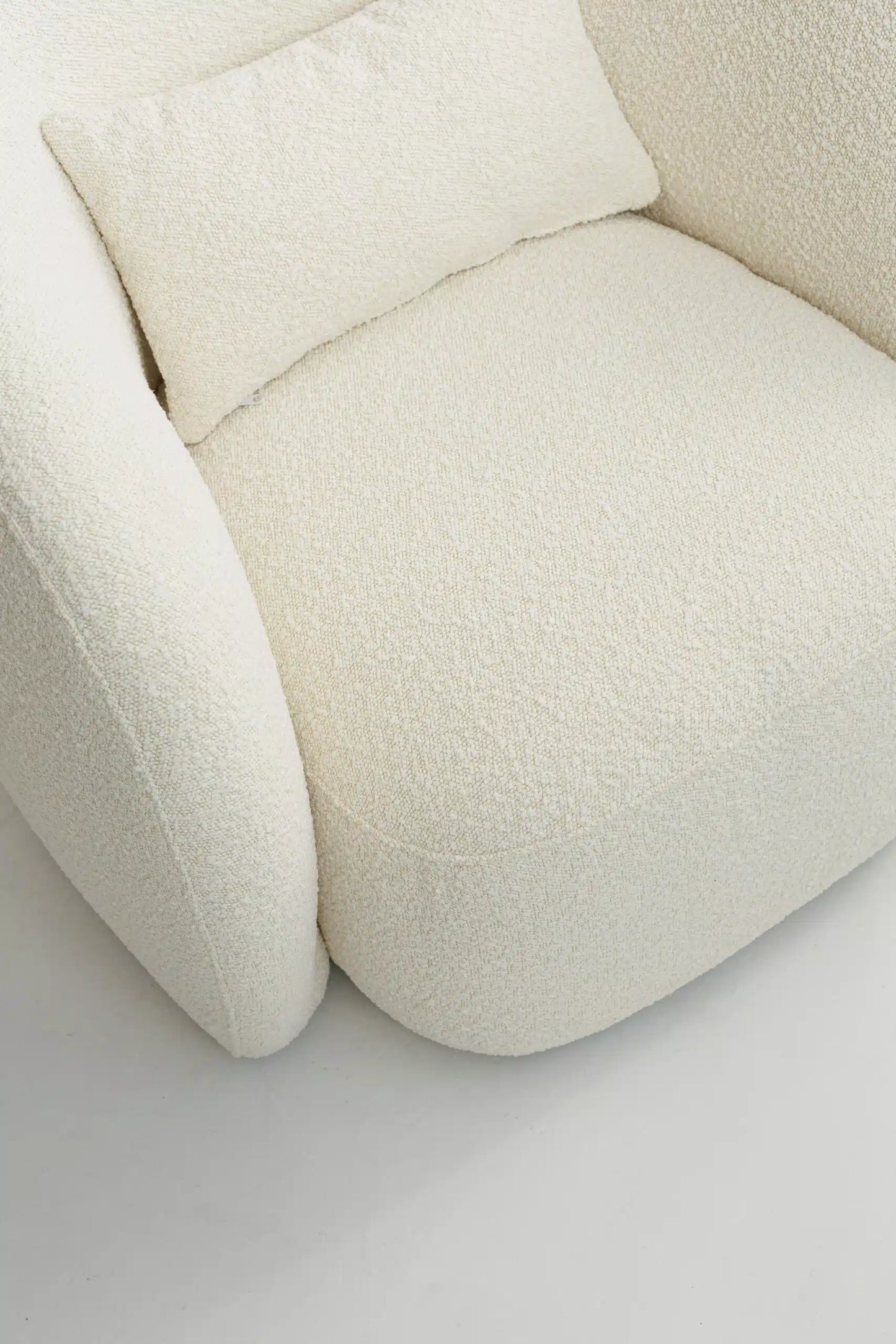 Close-up of a textured white bouclé armchair with cushions on a light background