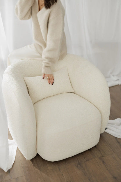 Person sitting on a large white bouclé armchair against a white curtain background