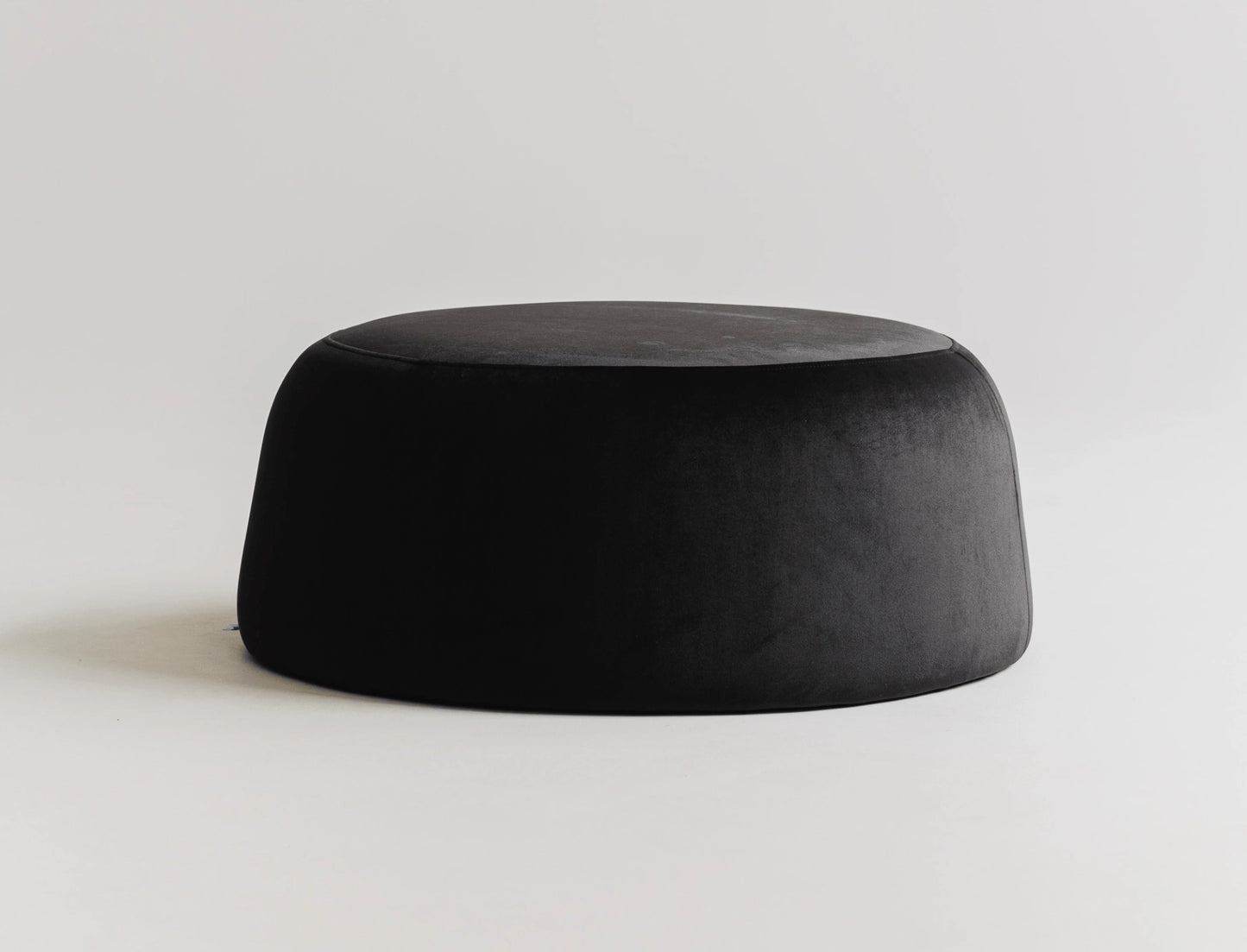 Round black velvet ottoman on a light gray background.