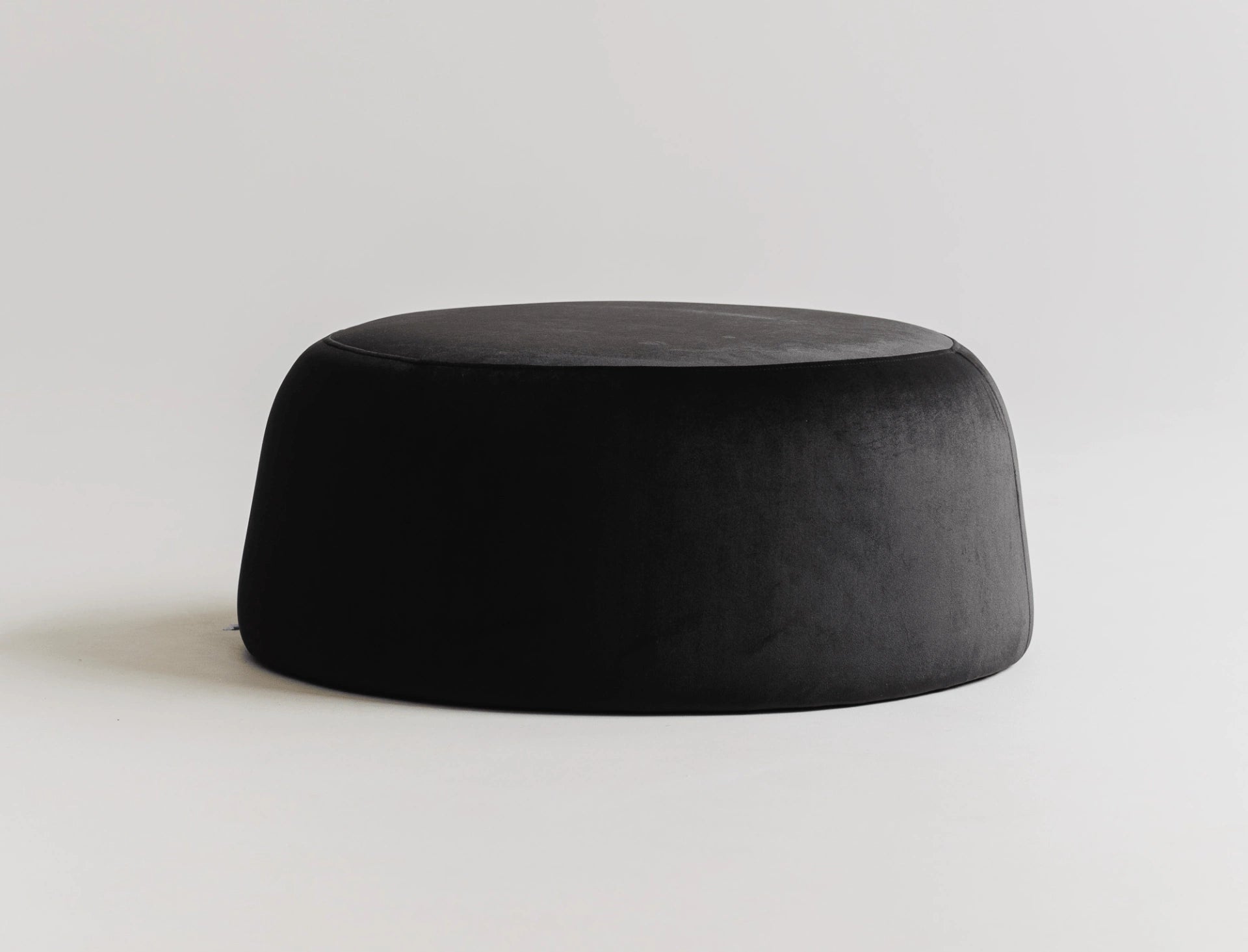 Round black velvet ottoman on a light gray background.