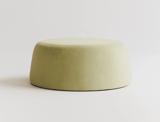 Round green velvet ottoman on a light gray background. 