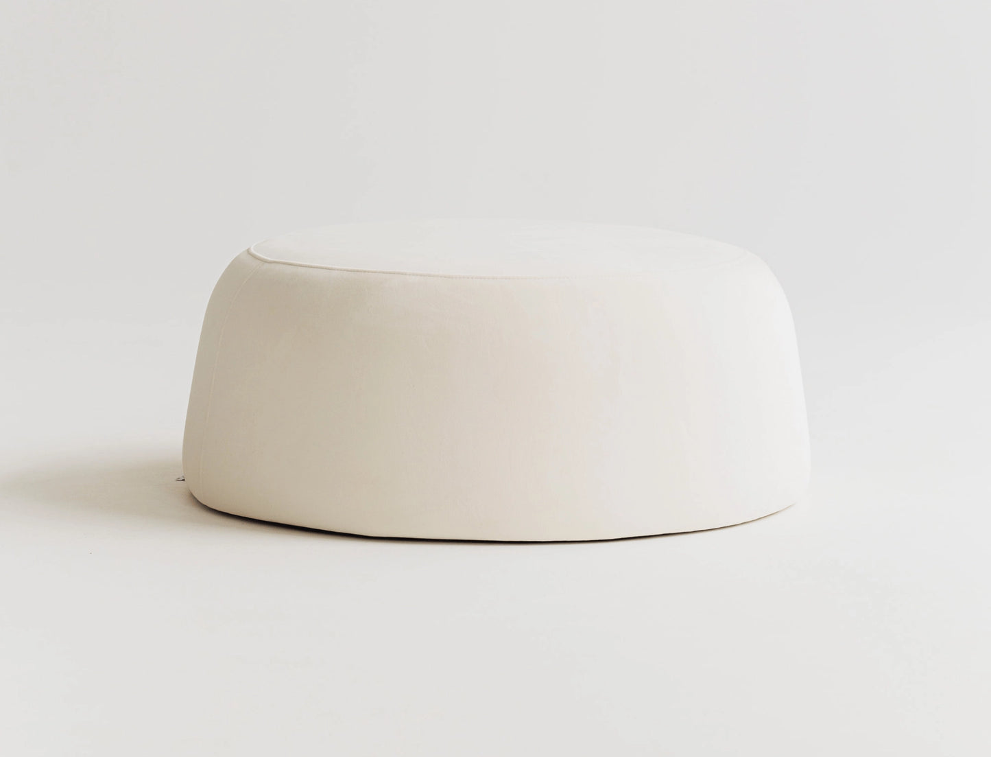 Round white velvet ottoman on a light gray background. 