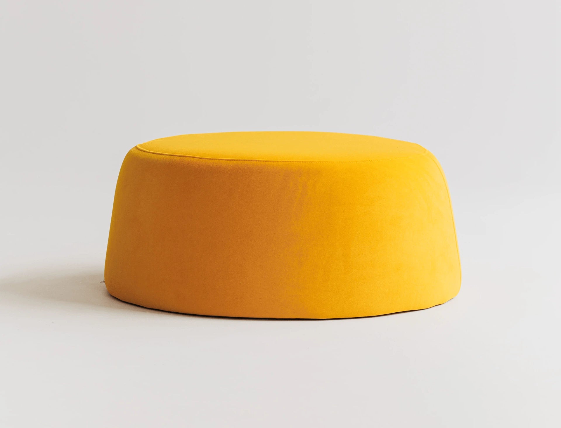 Round yellow velvet ottoman on a light gray background. 