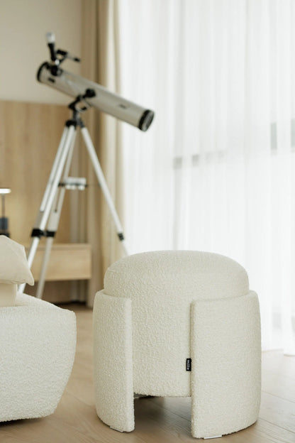 Telescope on a tripod next to a textured ottoman in a room with light-colored walls.