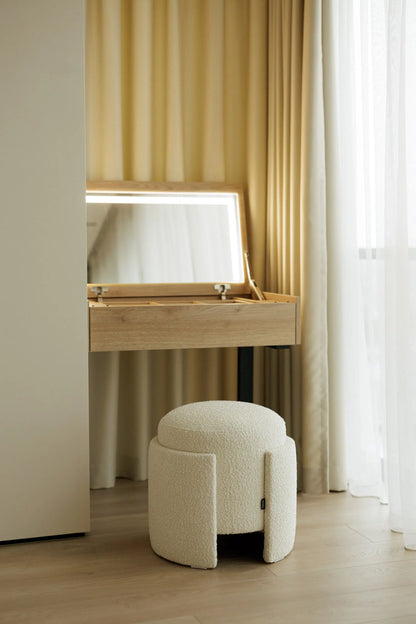 Wooden vanity table with mirror and white cushioned stool in a room with curtains.