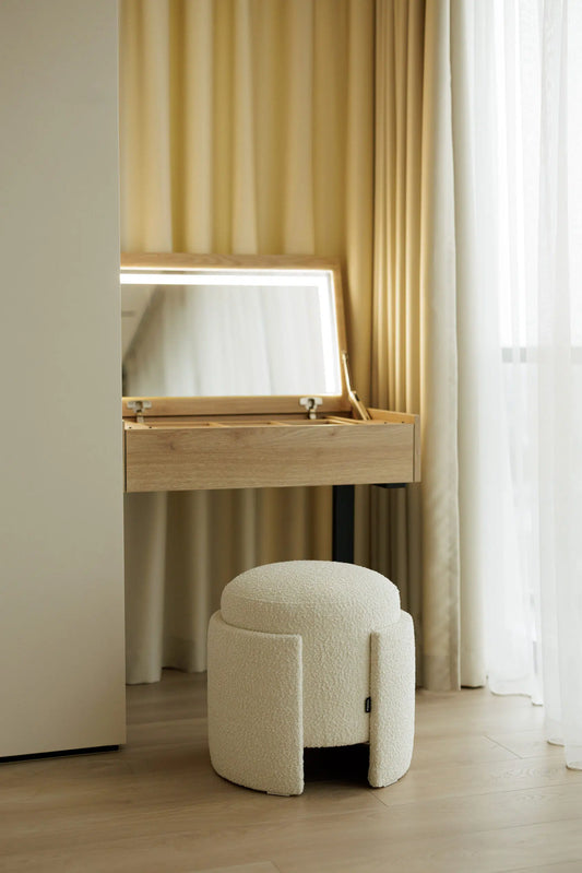 Wooden vanity table with mirror and white cushioned stool in a room with curtains.