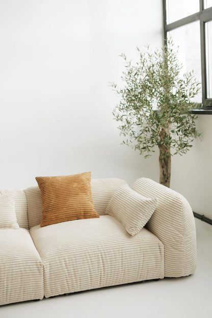 Beige sofa with a brown pillow and a potted plant in a minimalistic room.