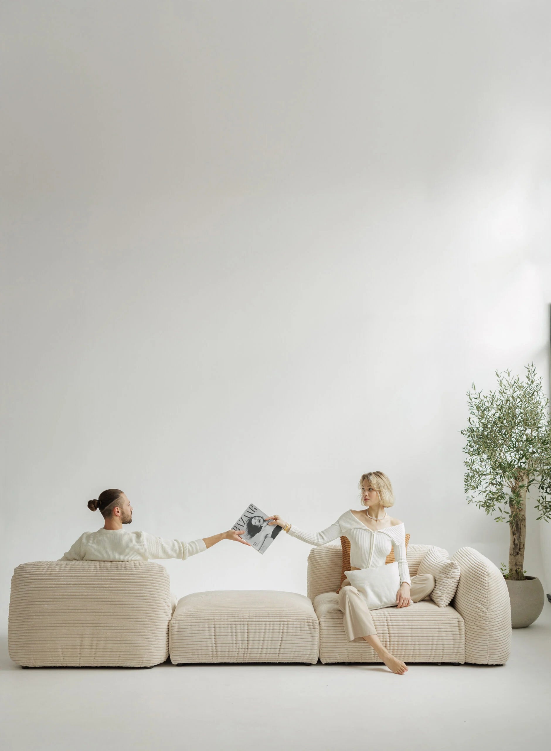 Two people sitting on a modern beige sofa in a minimalistic room with a plant.