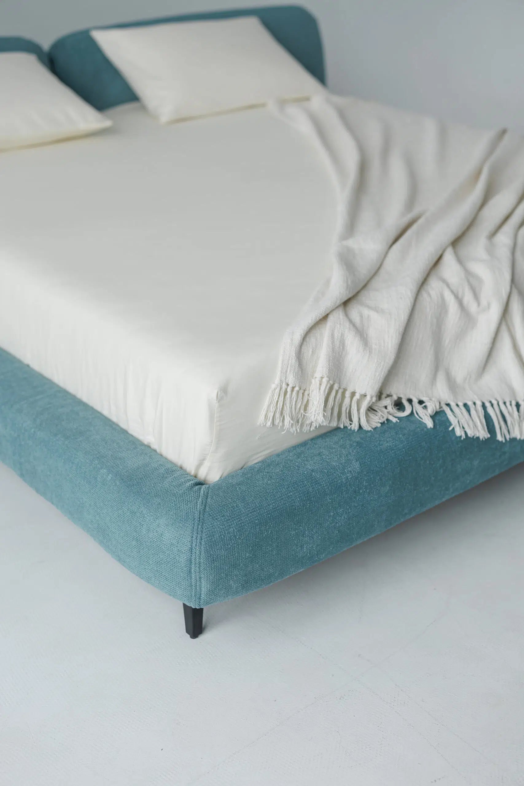Blue upholstered bed with white mattress and blanket on a plain background