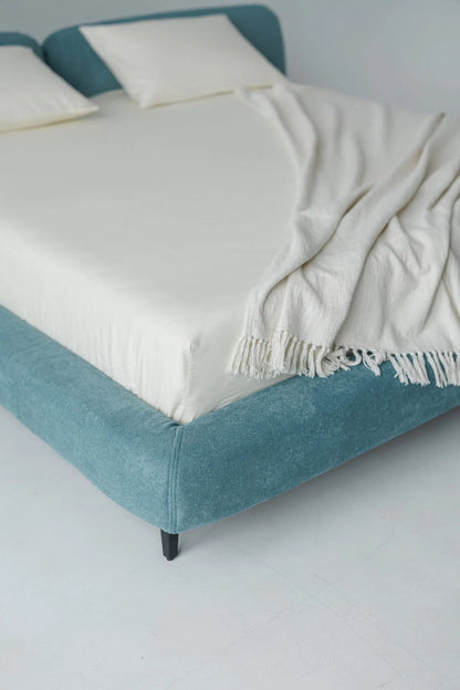 Blue upholstered bed with white mattress and blanket on a plain background