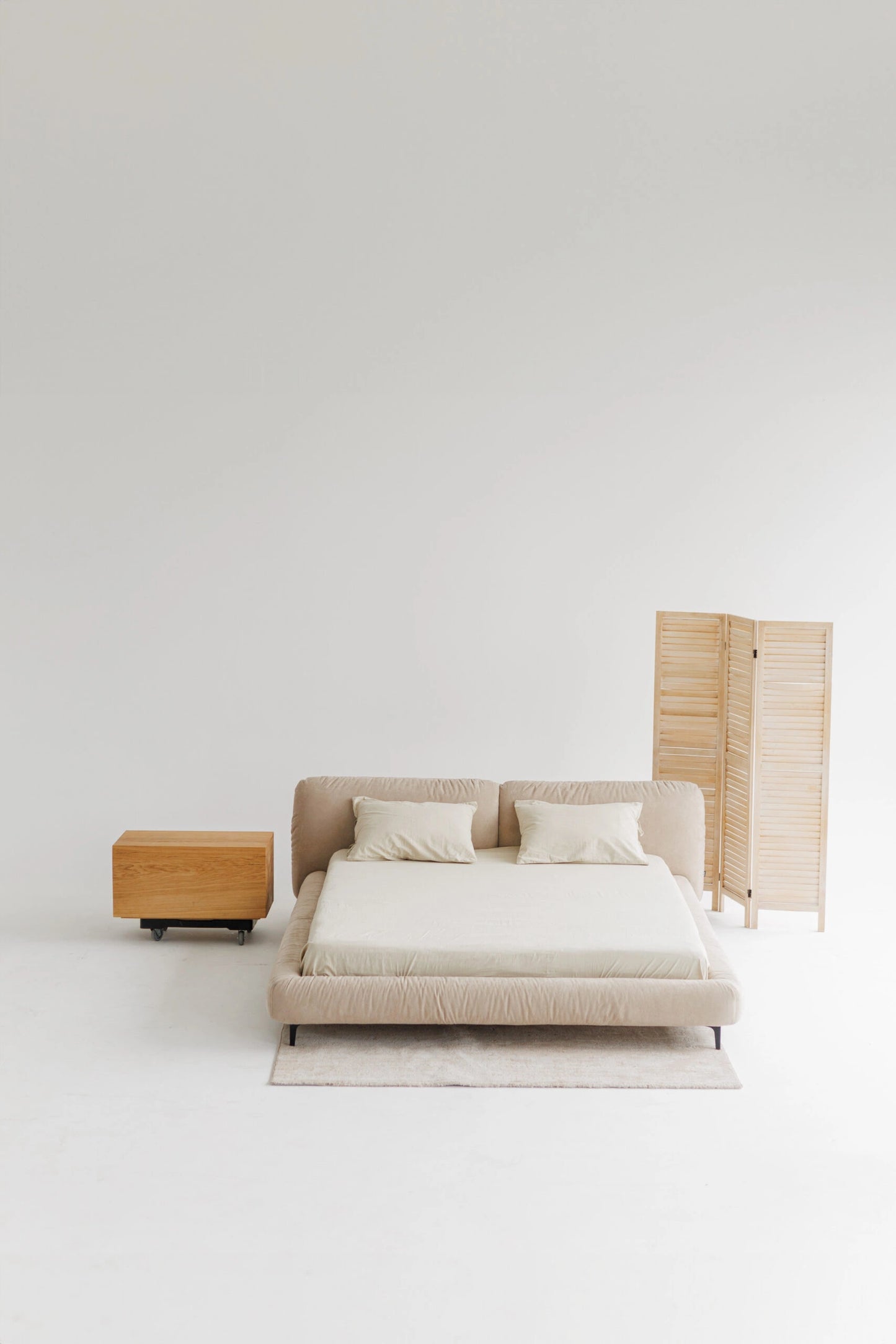 Modern beige upholstered bed with big headboard and side table against a white wall