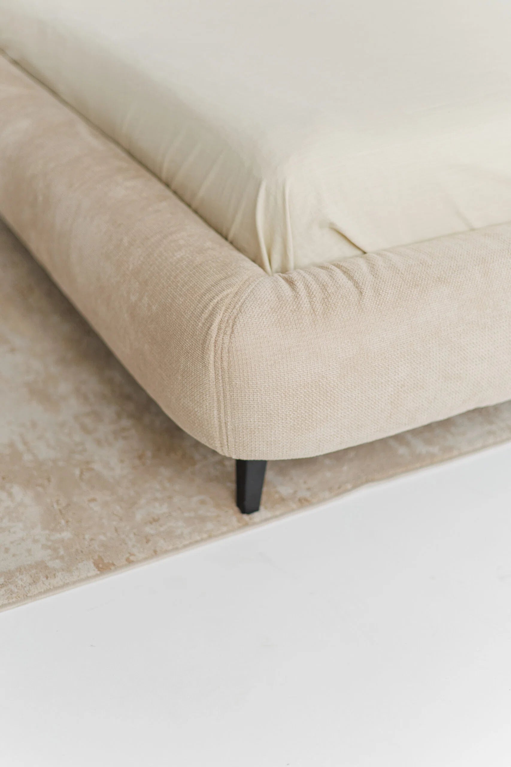 Beige designer bed with black legs on a light-colored floor