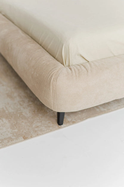 Beige designer bed with black legs on a light-colored floor