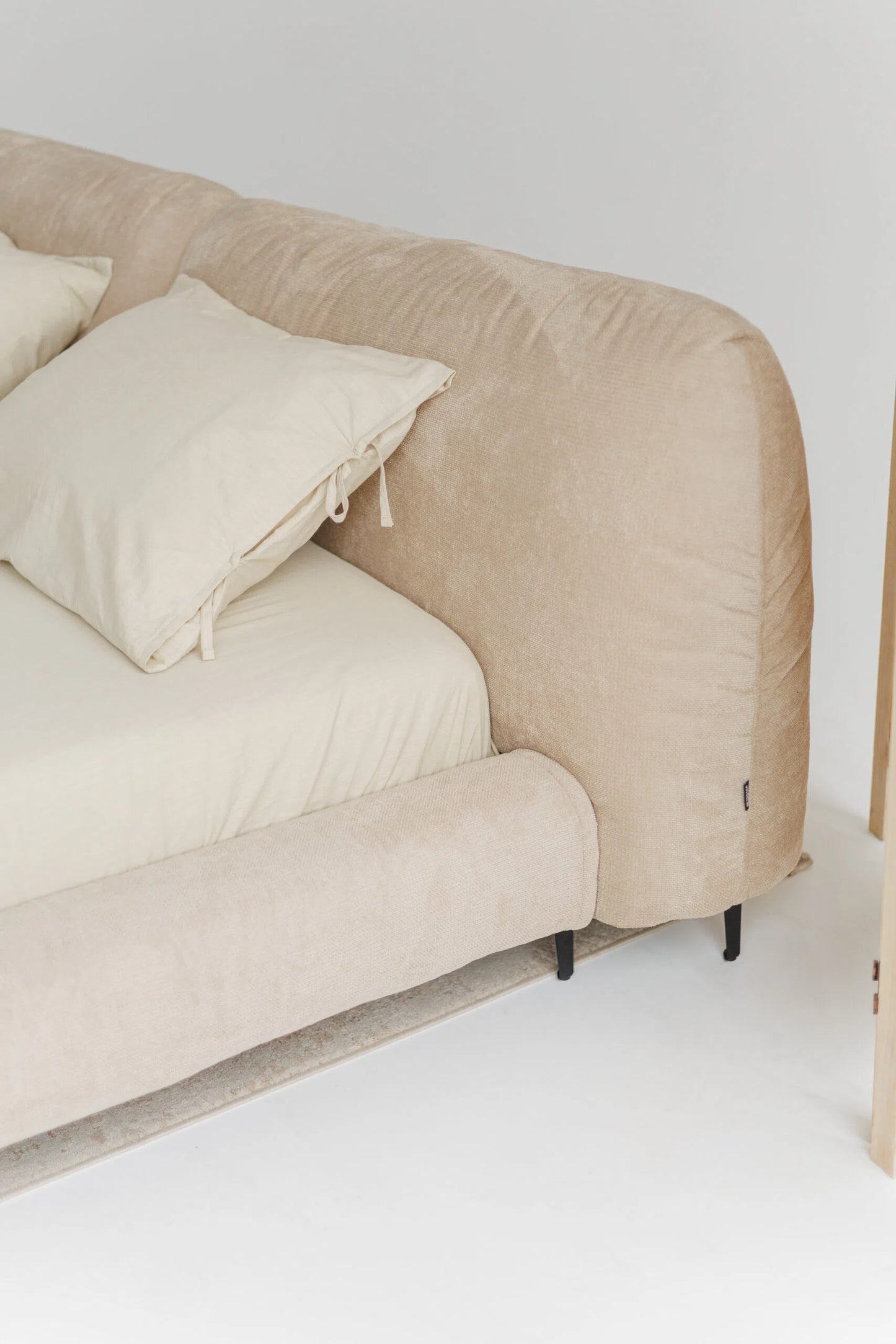 Beige designer bed with white cushions on a white floor and wall