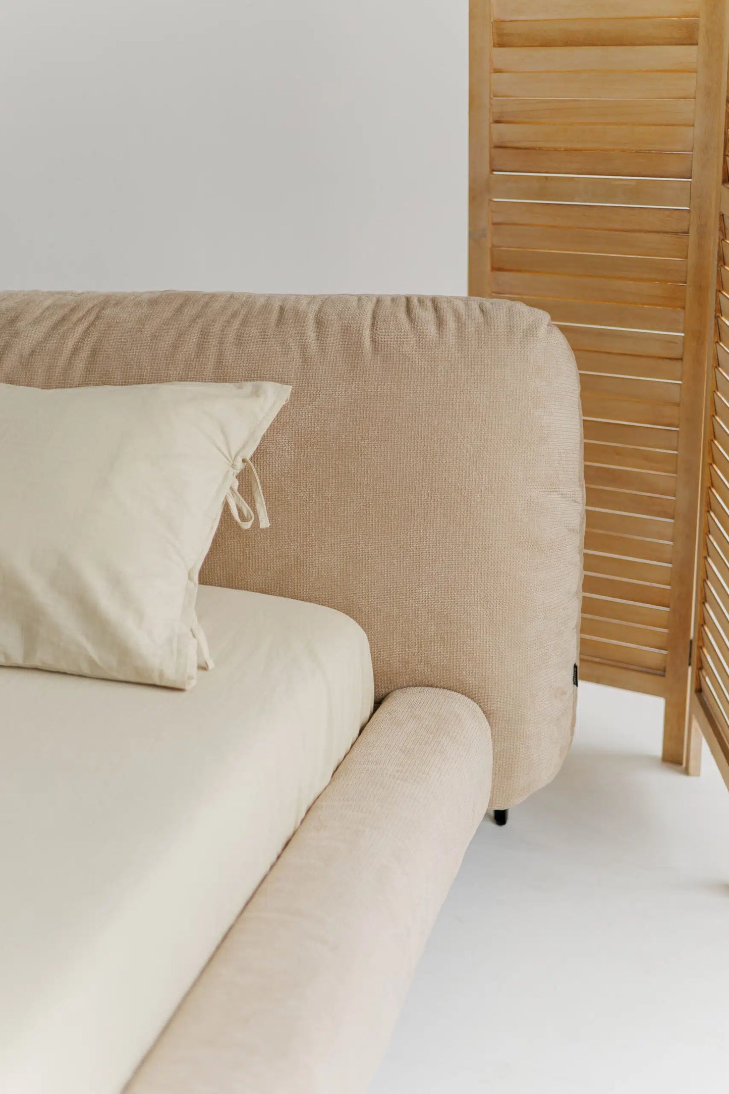 Beige upholstered bed with a wooden screen in a minimalistic room