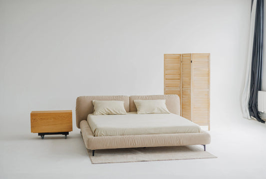 Beige upholstered bed with puffy headboard and nightstand in a minimalistic room