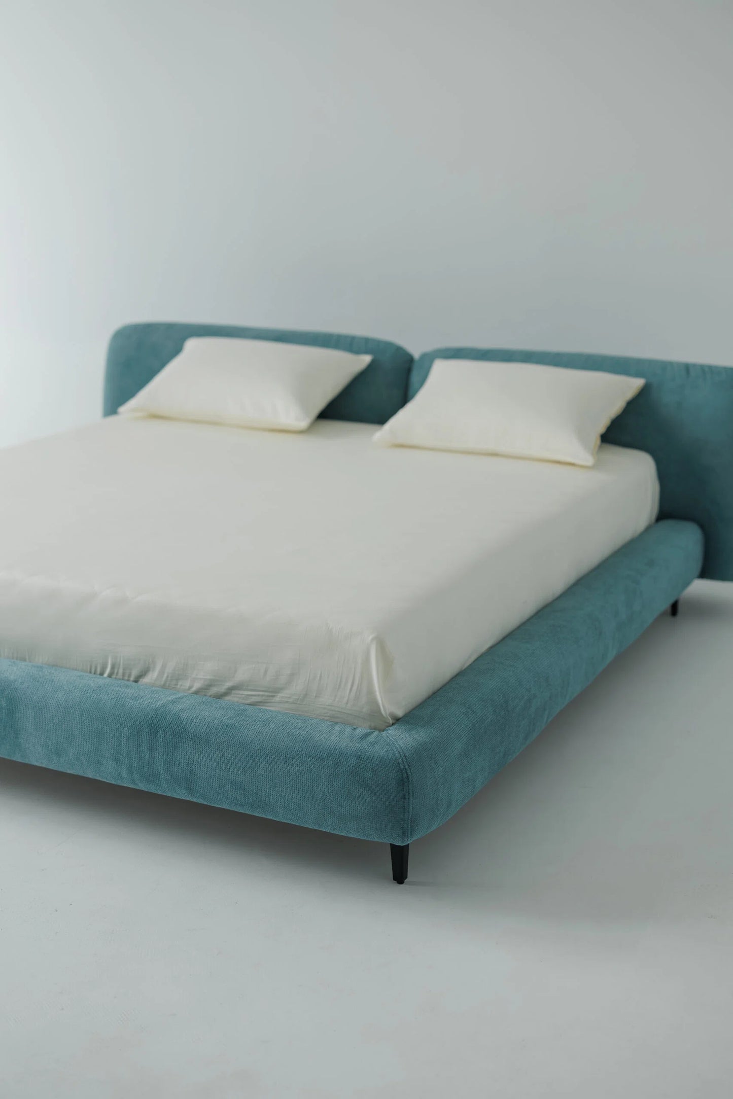 Blue upholstered bed with white bedding against a plain wall