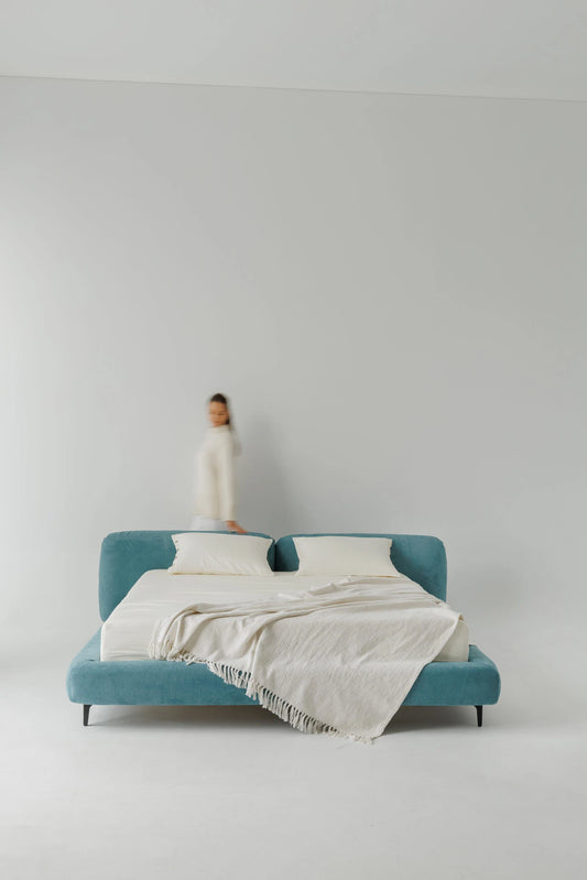 Blue designer bed with a white blanket on a plain background