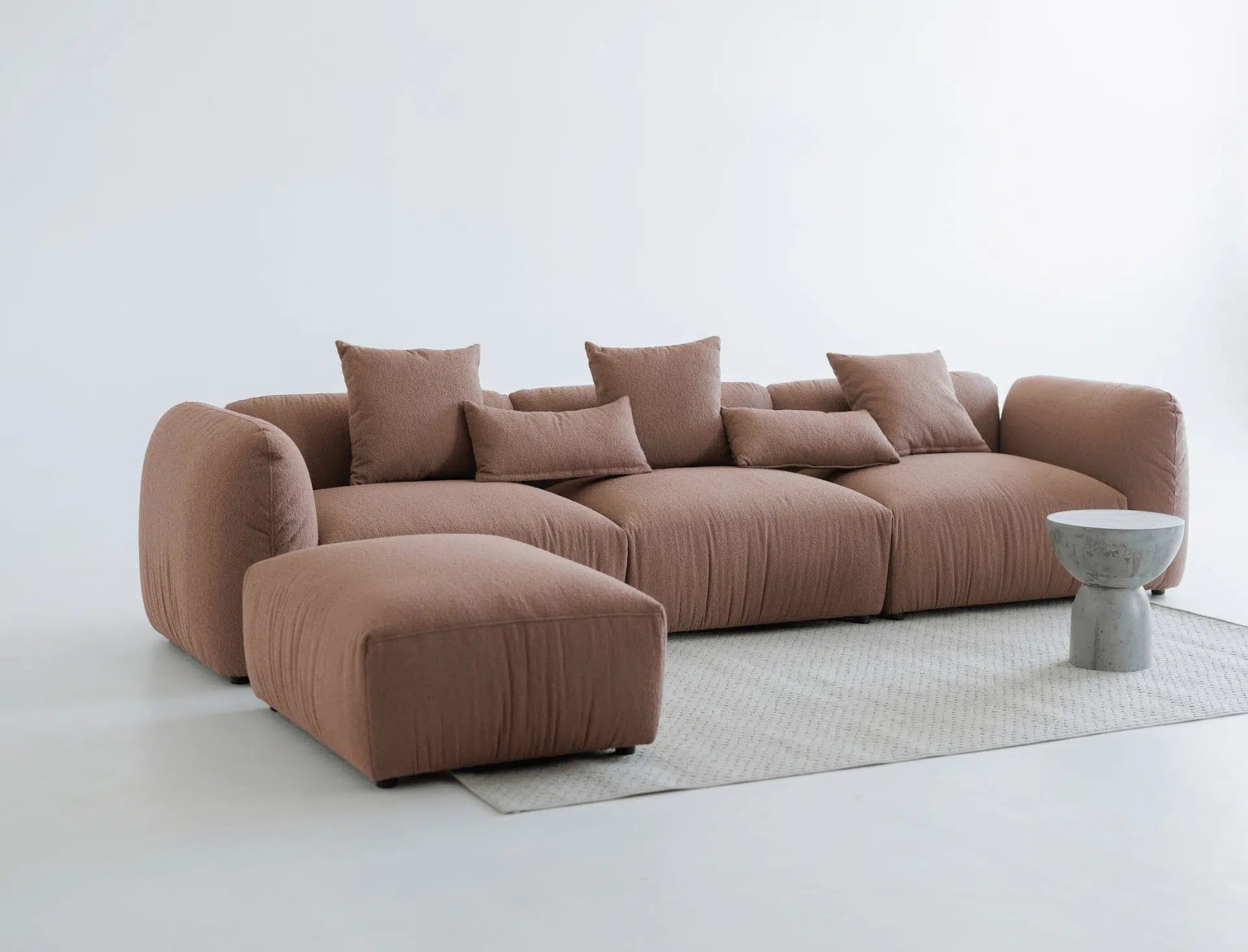 Brown sectional sofa with a matching ottoman on a light gray floor with a white wall background.