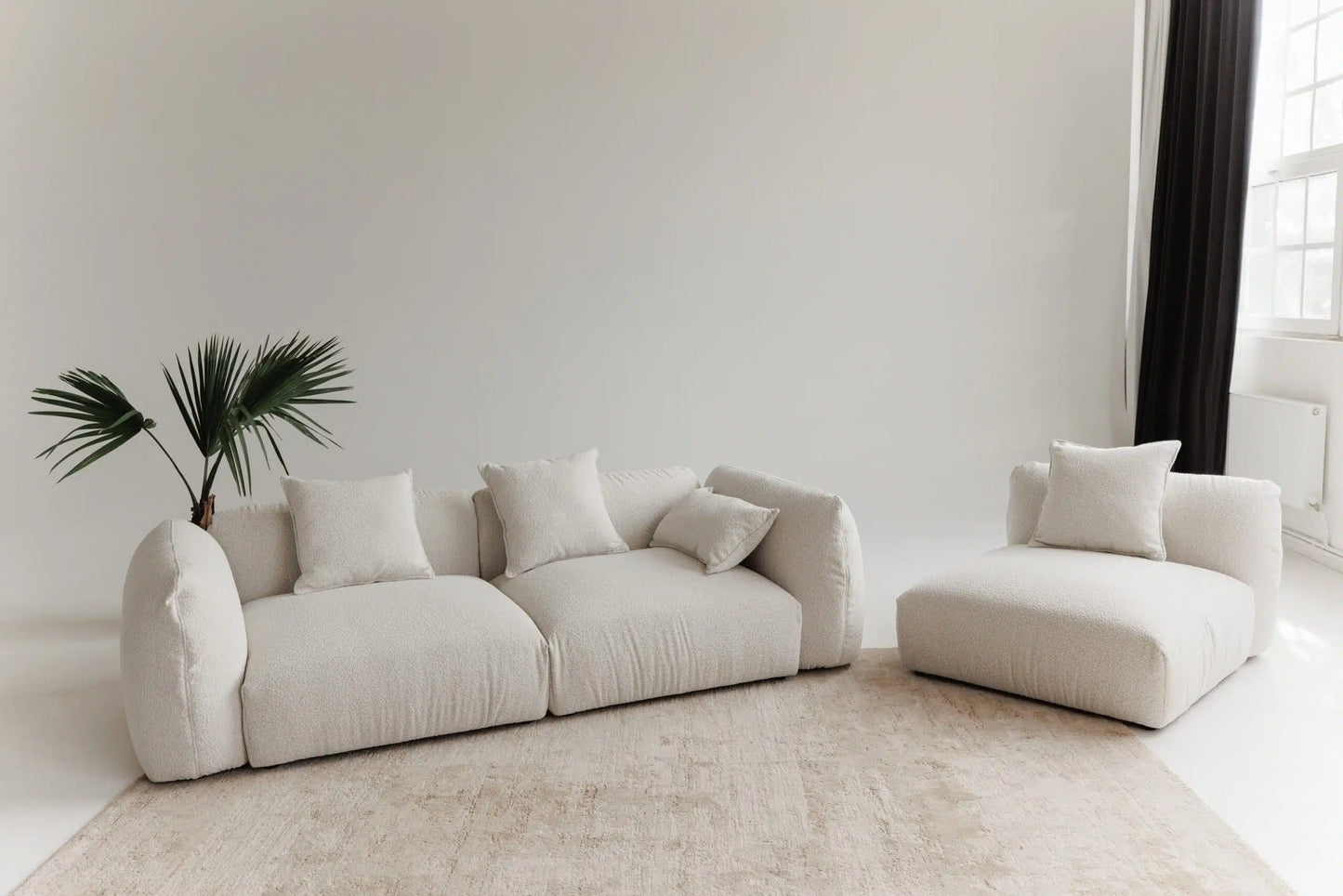 White sofa with modular system and armchair in a minimalistic room with a plant.