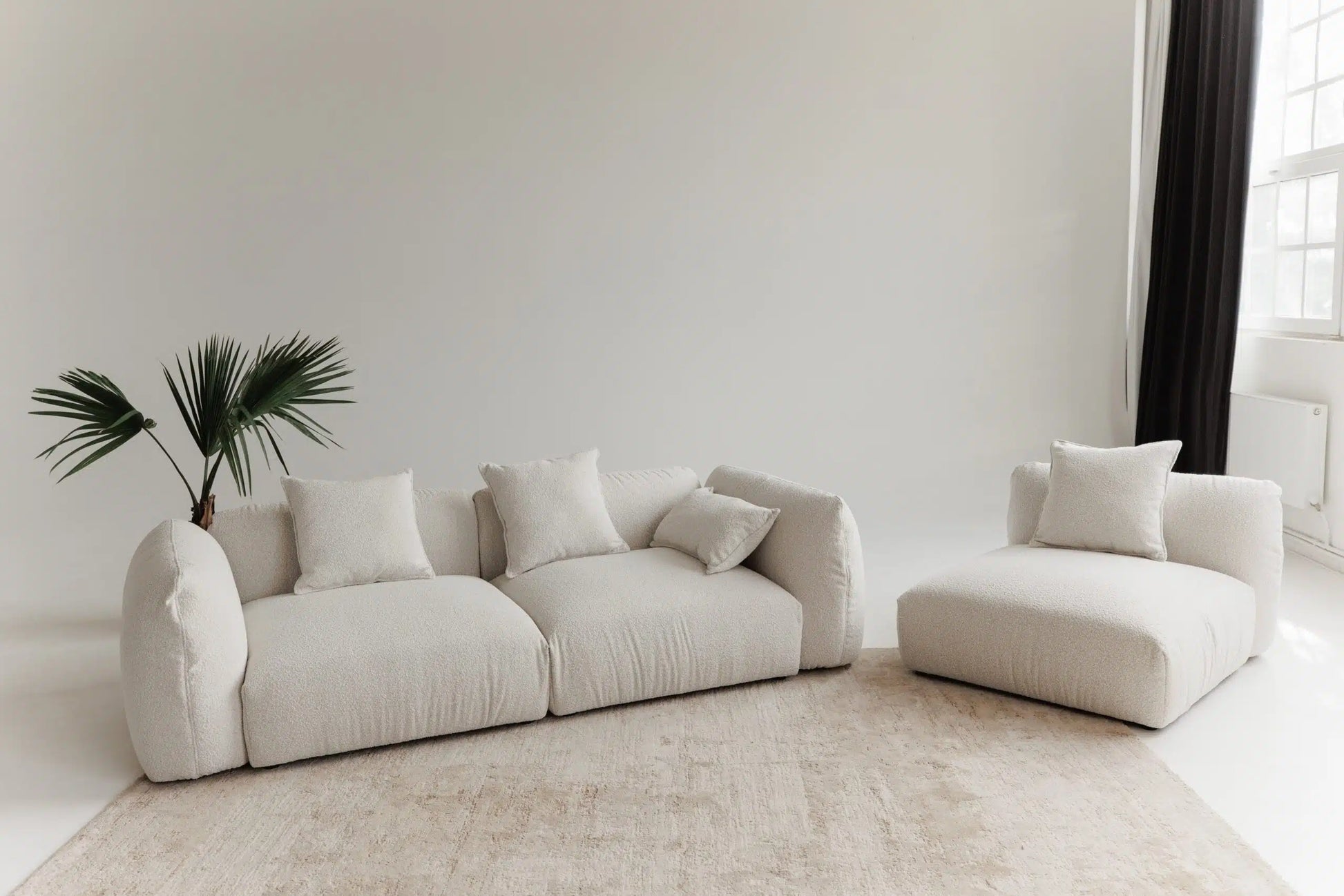 White sofa with modular system and armchair in a minimalistic room with a plant.