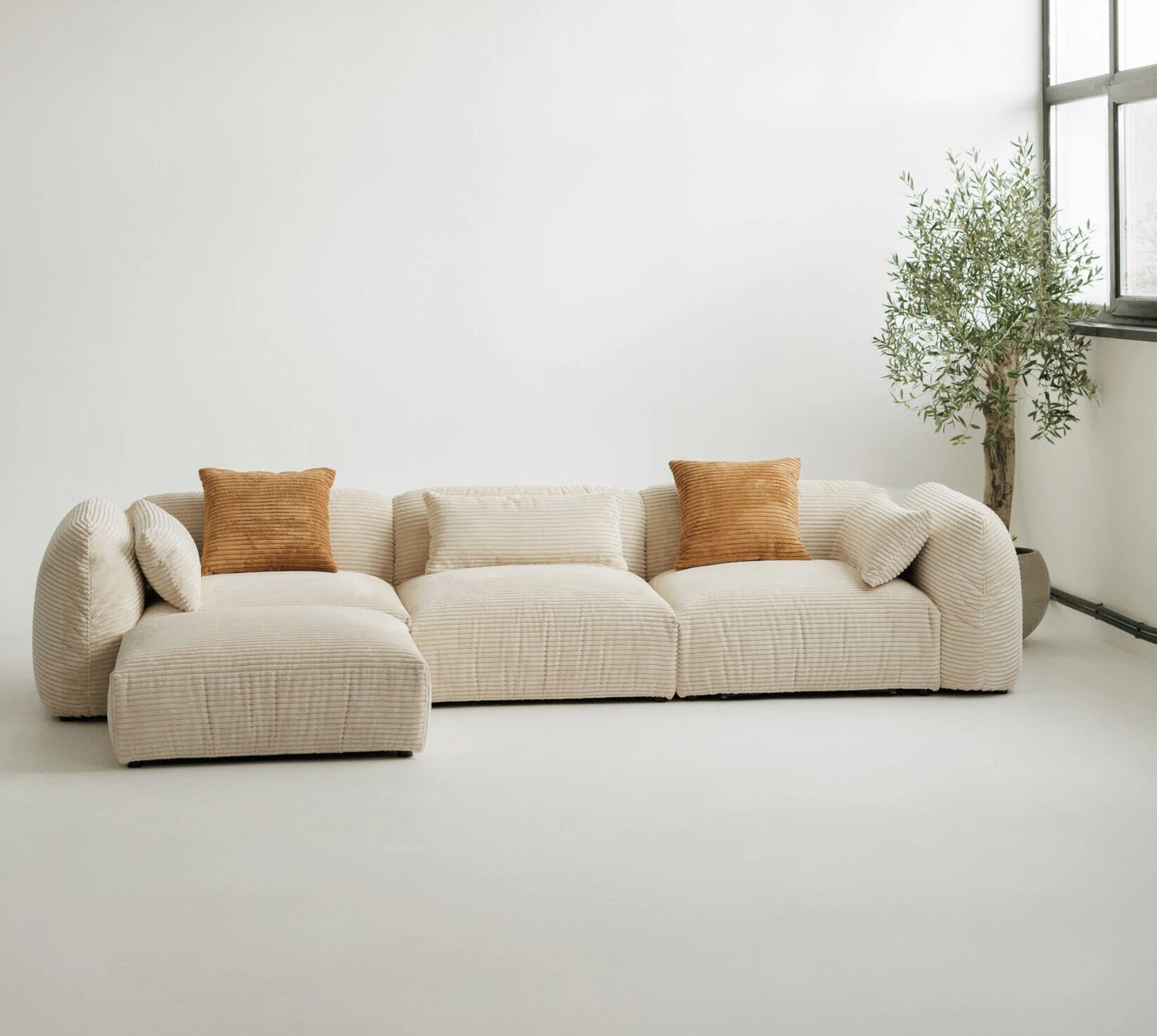 Beige sectional cord sofa in with brown cushions in a minimalistic room.