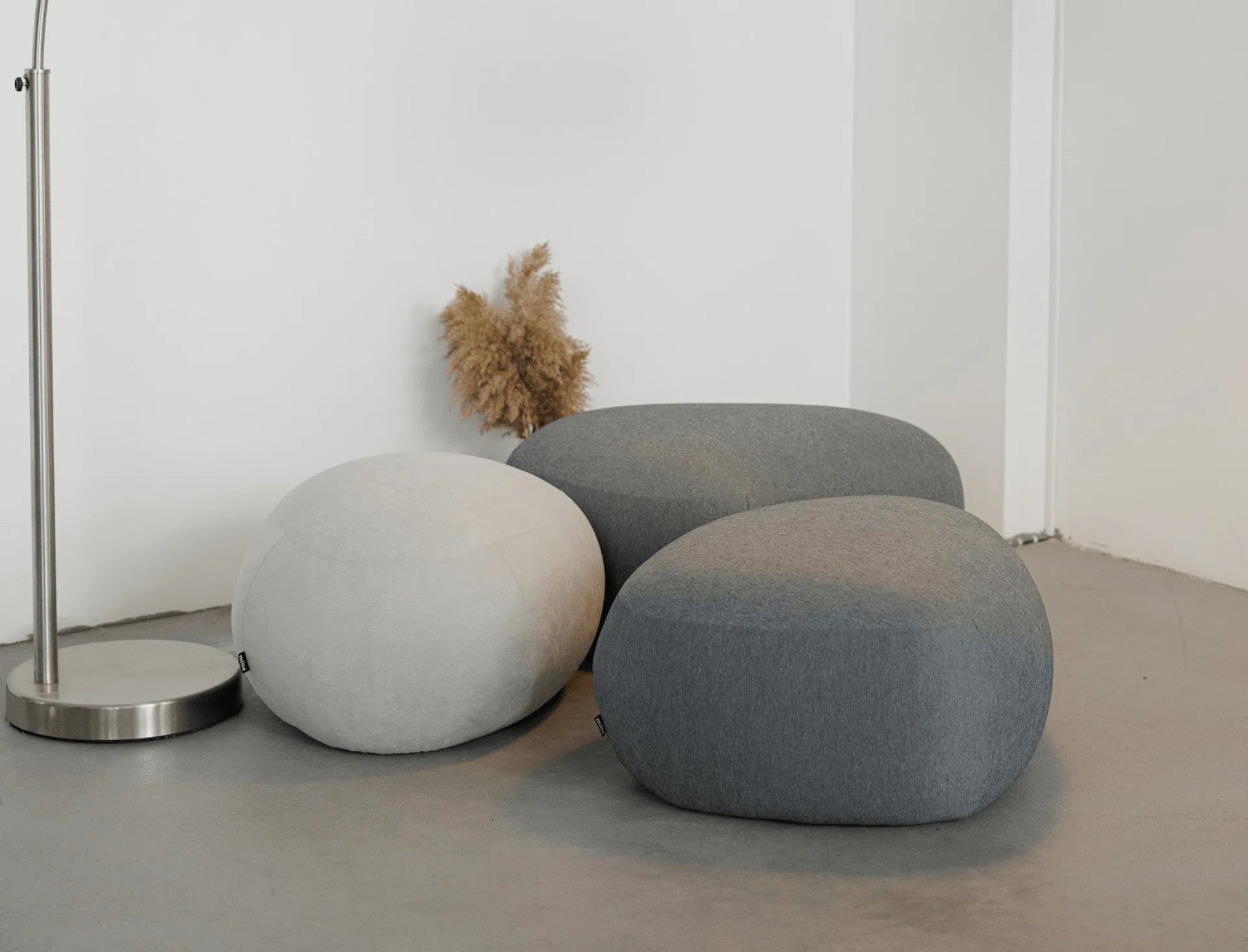 Three gray and white textured poufs on a concrete floor with a minimal background.