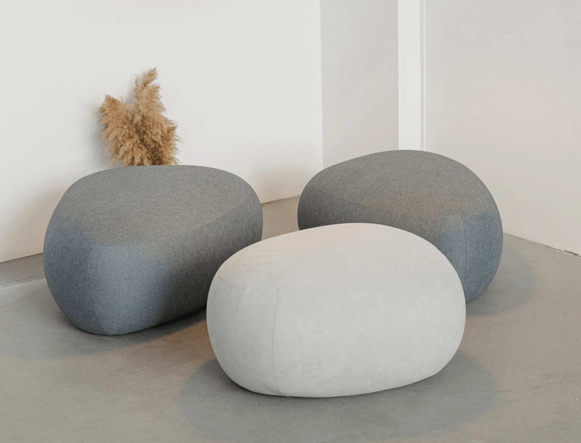 Three gray and white textured poufs on a light gray floor with a white wall background.