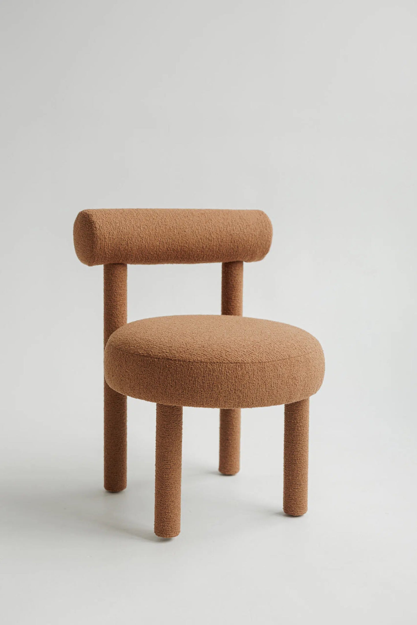 Brown upholstered bouclé chair with a minimalist design on a light gray background
