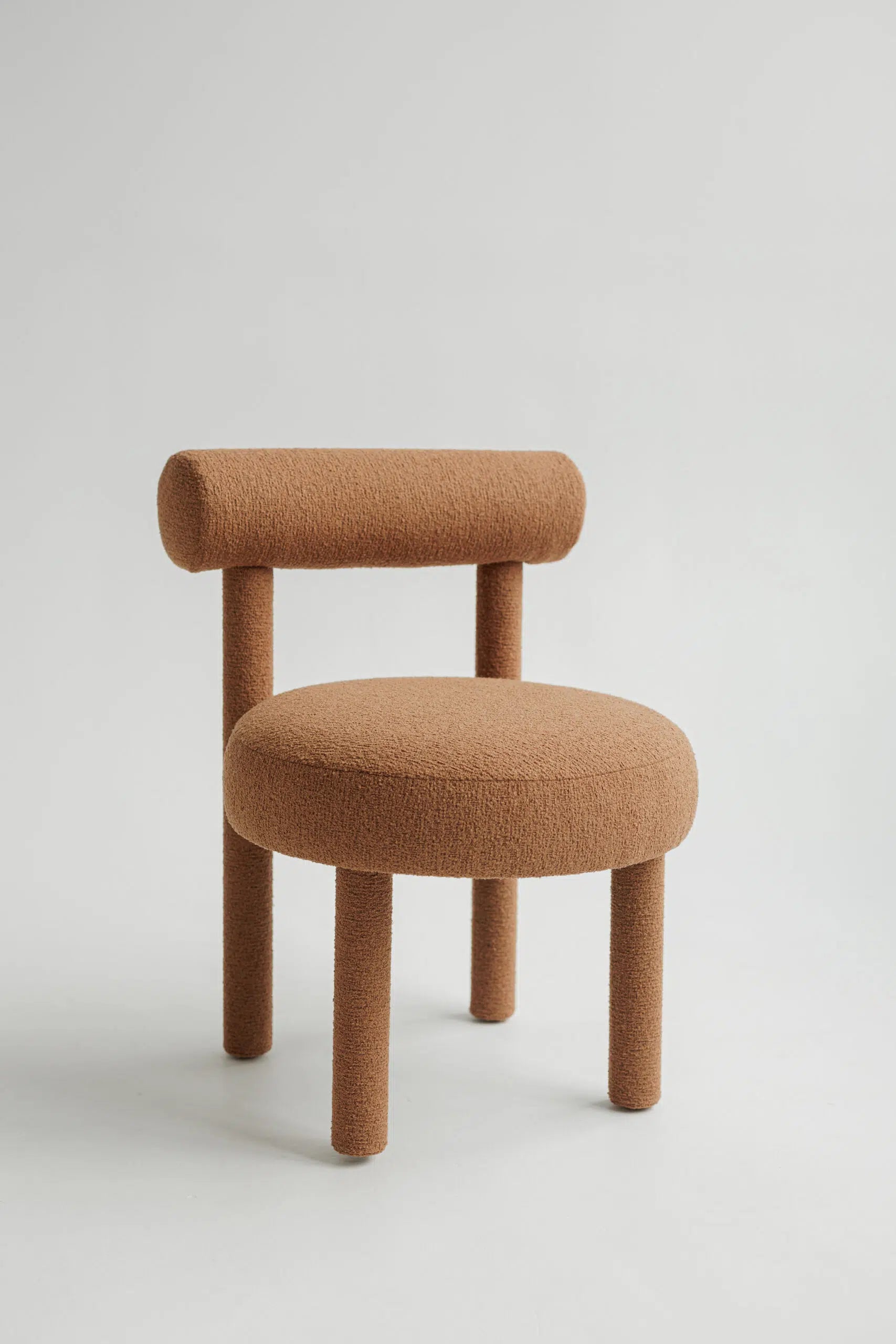 Brown upholstered bouclé chair with a minimalist design on a light gray background