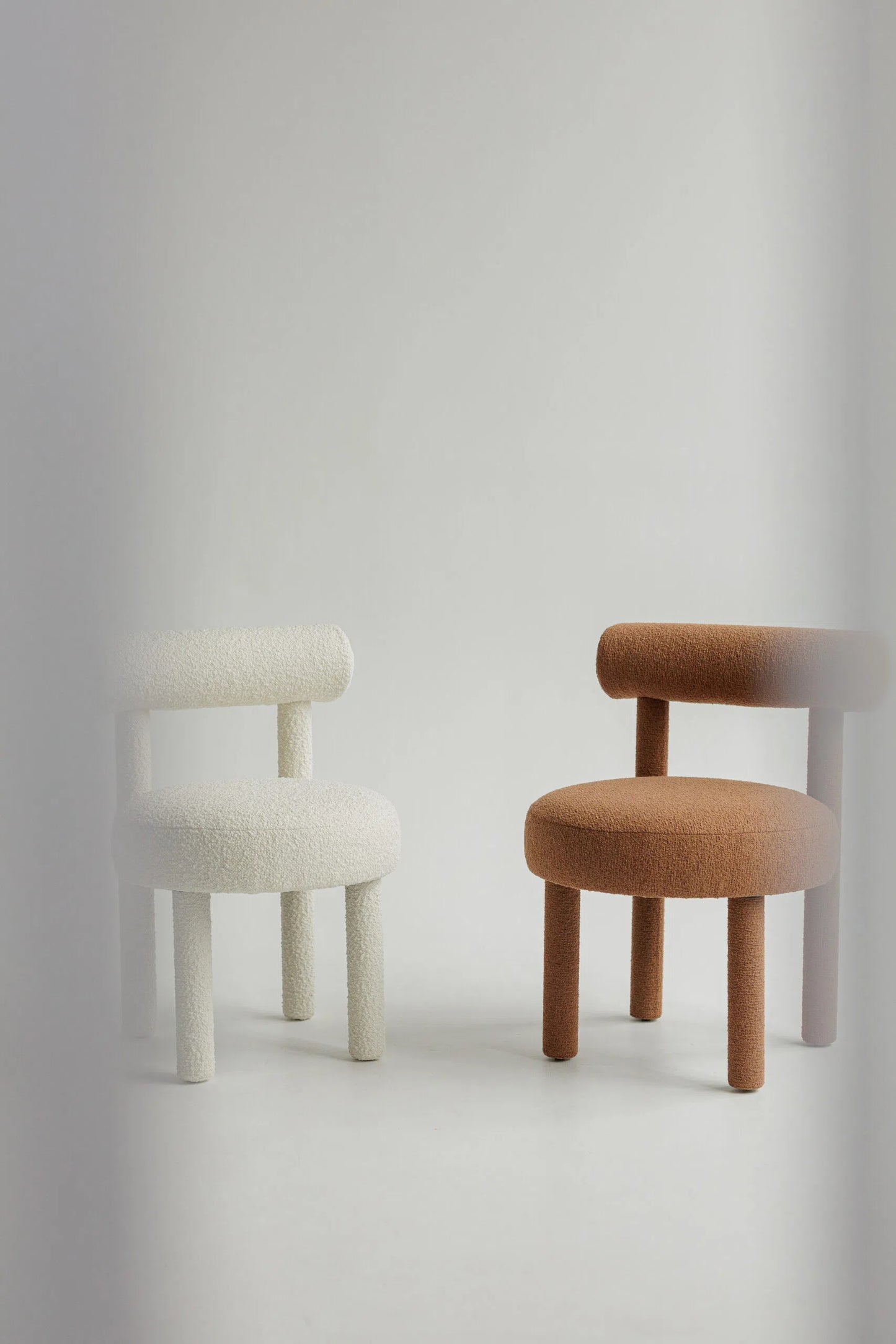 Two upholstered bouclé chairs, one white and one brown, on a light gray background