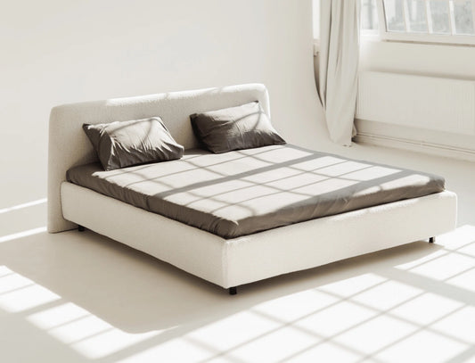 Modern bed with white frame and gray mattress in a bright room.