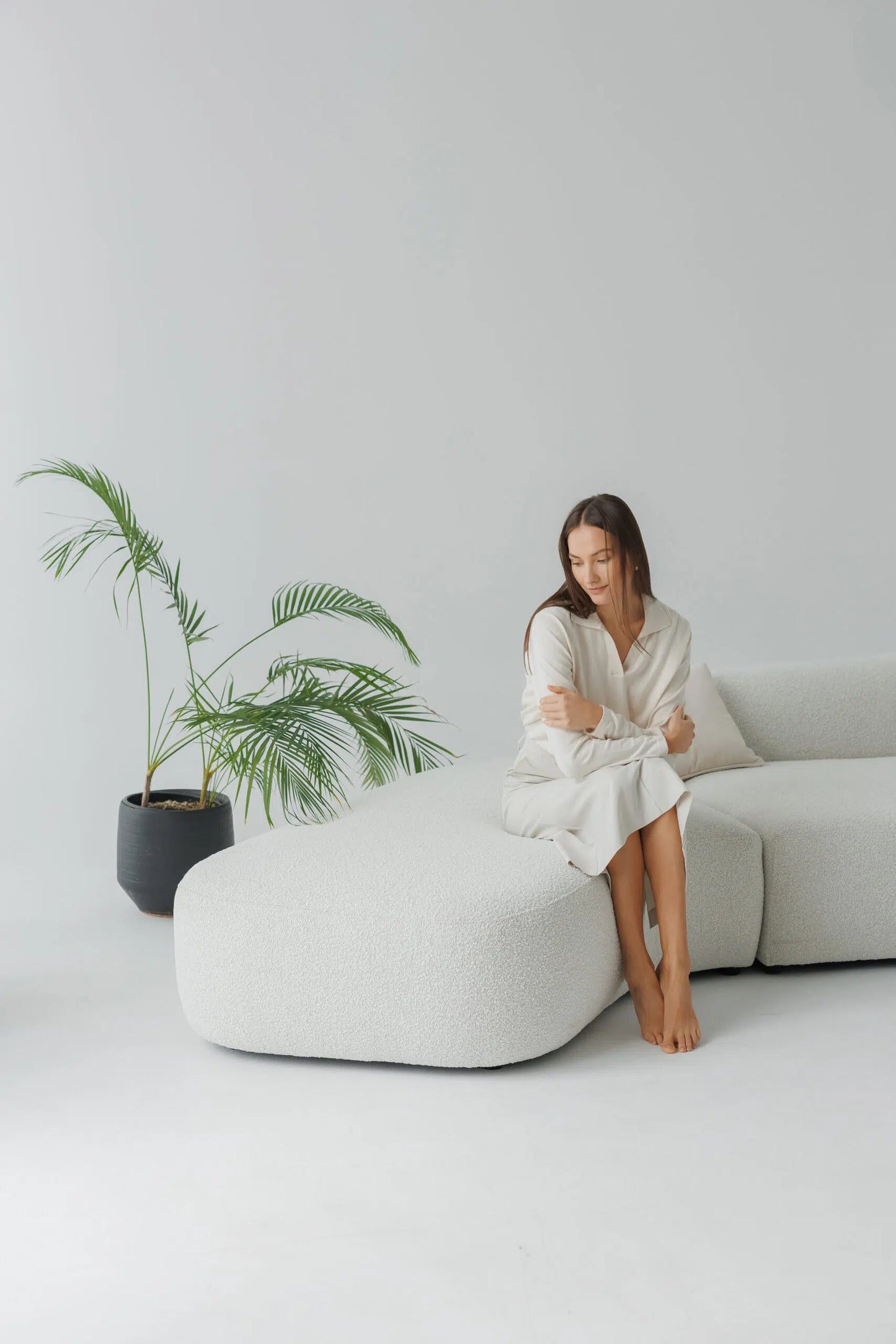 Woman sitting on a modern white boucle sofa with a plant in the background